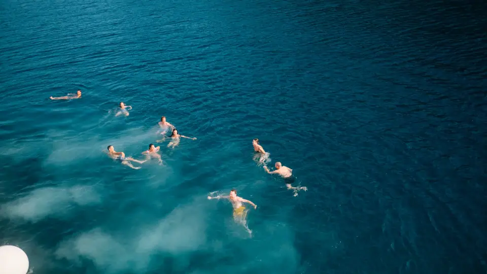 Swimmers and pale wakes scattered across blue water.