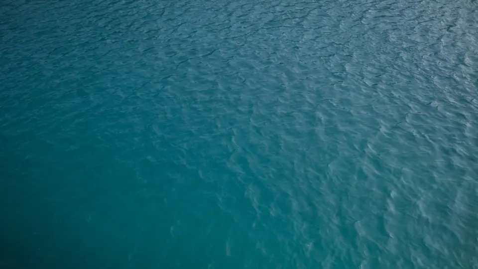 Fine ripples cover a surface shifting from teal to silver.