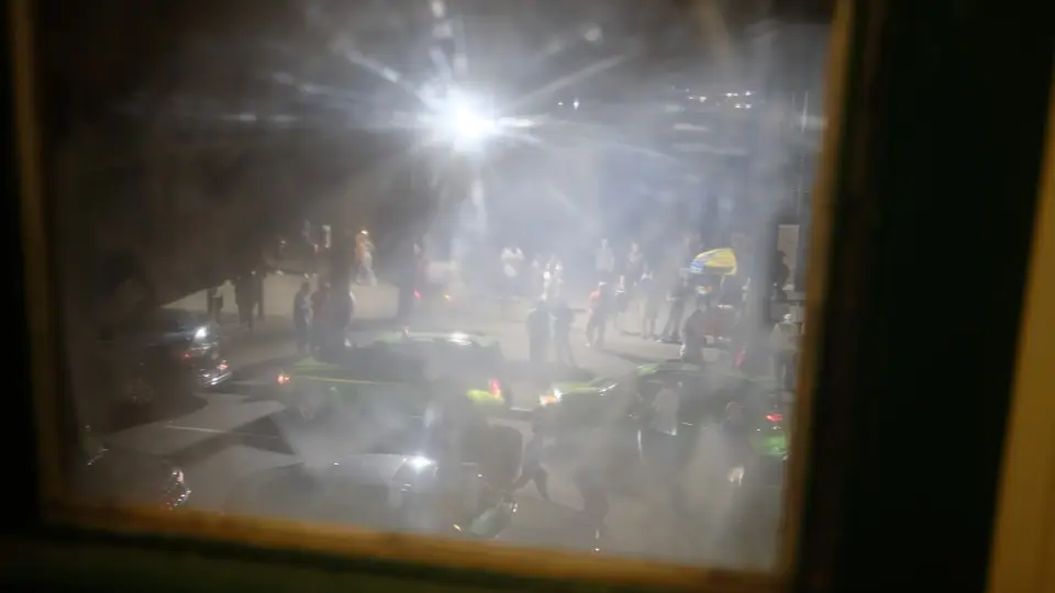 A night gathering seen through a hazy window with layered light and reflections.