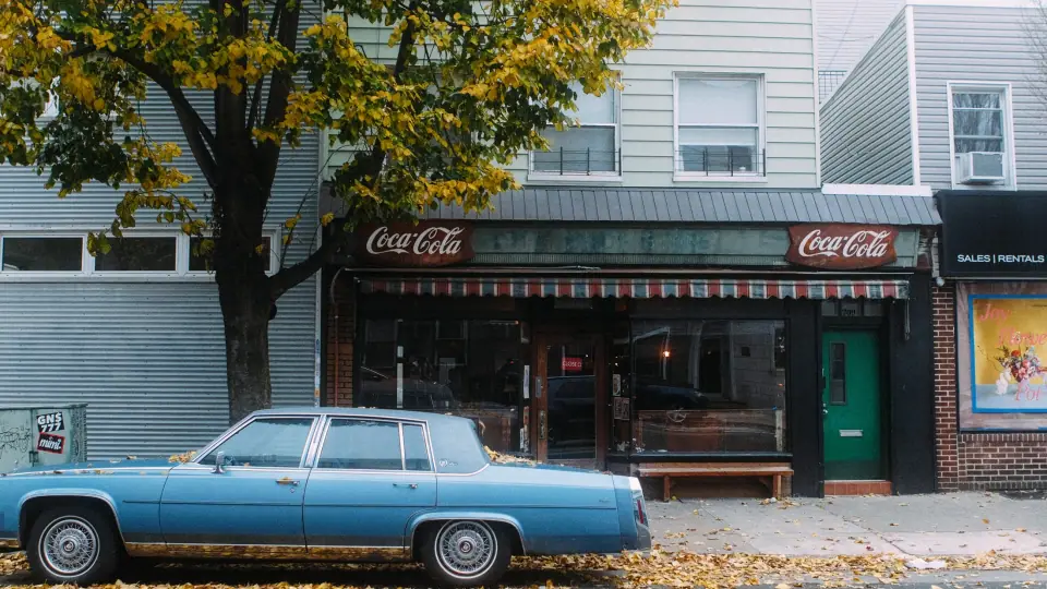 A blue car sits alongside a storefront.