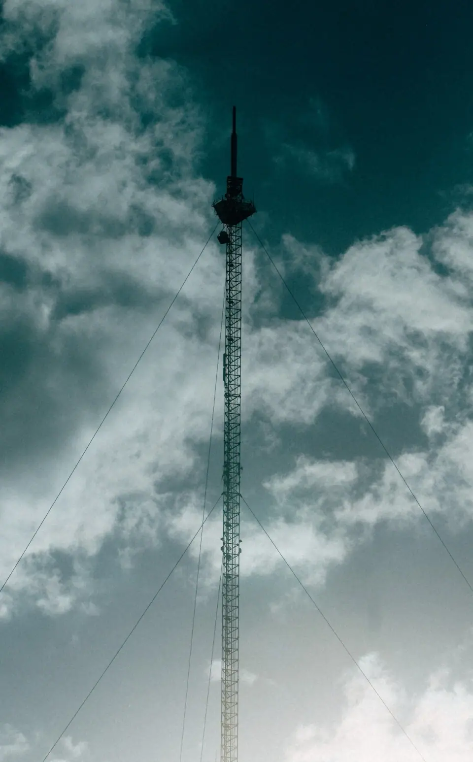 A slender tower rises through clouds in a vertical frame.