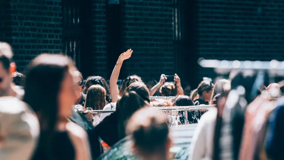 A single raised hand emerges above layers of sunlit heads.