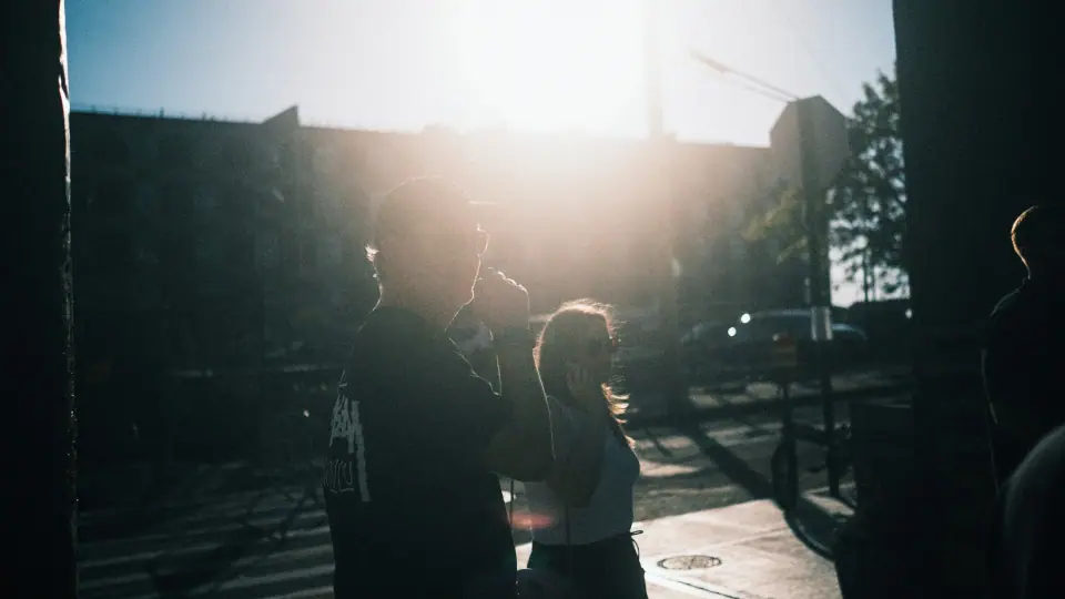 Low sunlight silhouettes people gathered in the street.