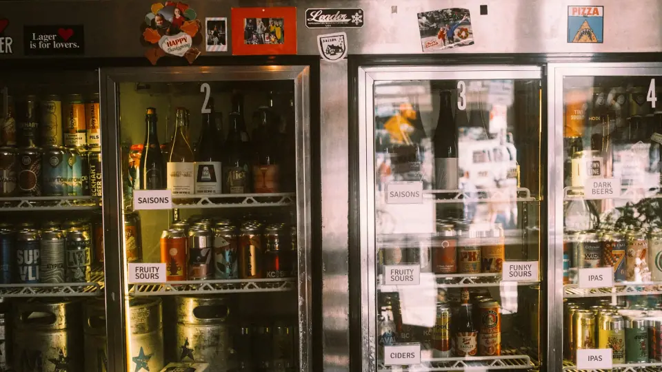 Reflections and rows of bottles form a layered grid inside a cabinet.