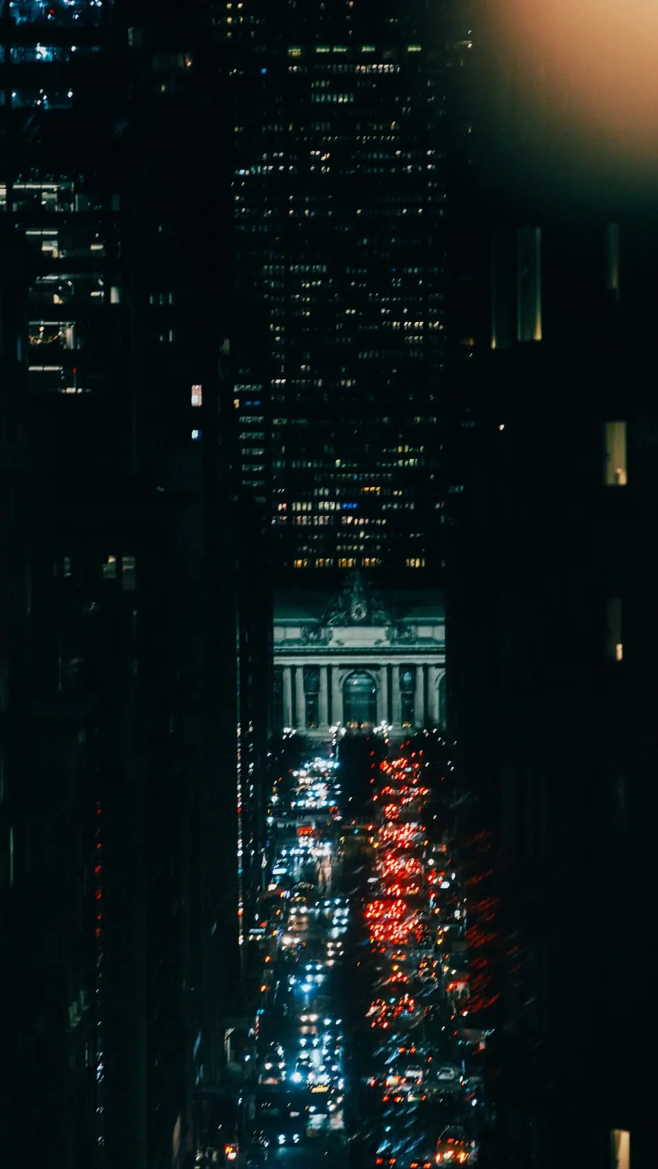 Red and white city lights appear through a narrow vertical opening in darkness.