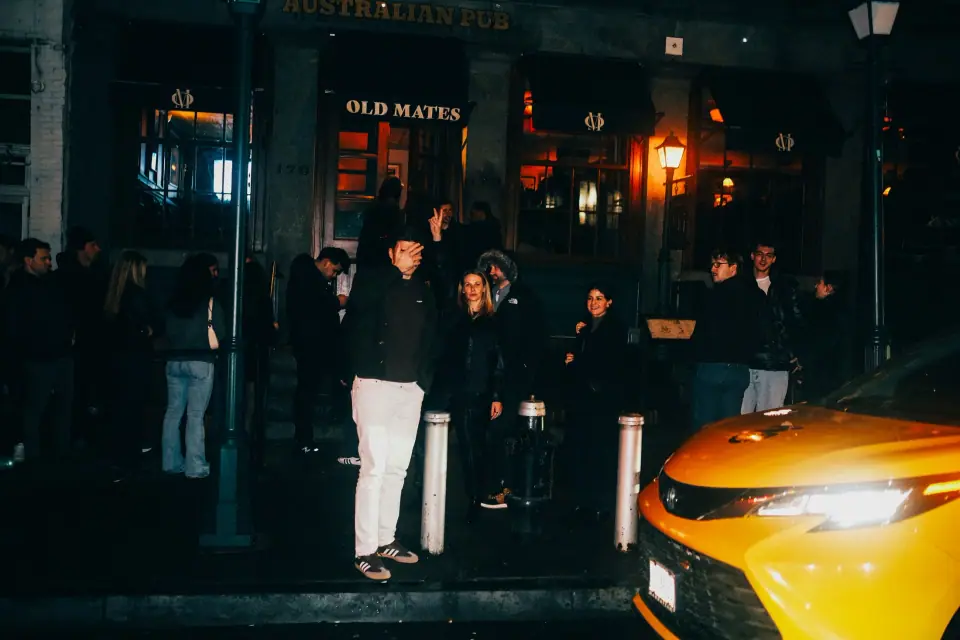 A yellow car stands out beside a dark street gathering.