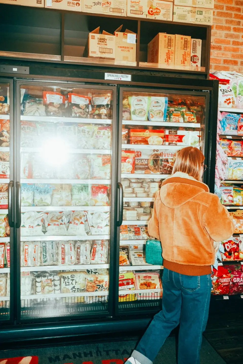 An orange figure stands among repeating shop shelves in cool tones.